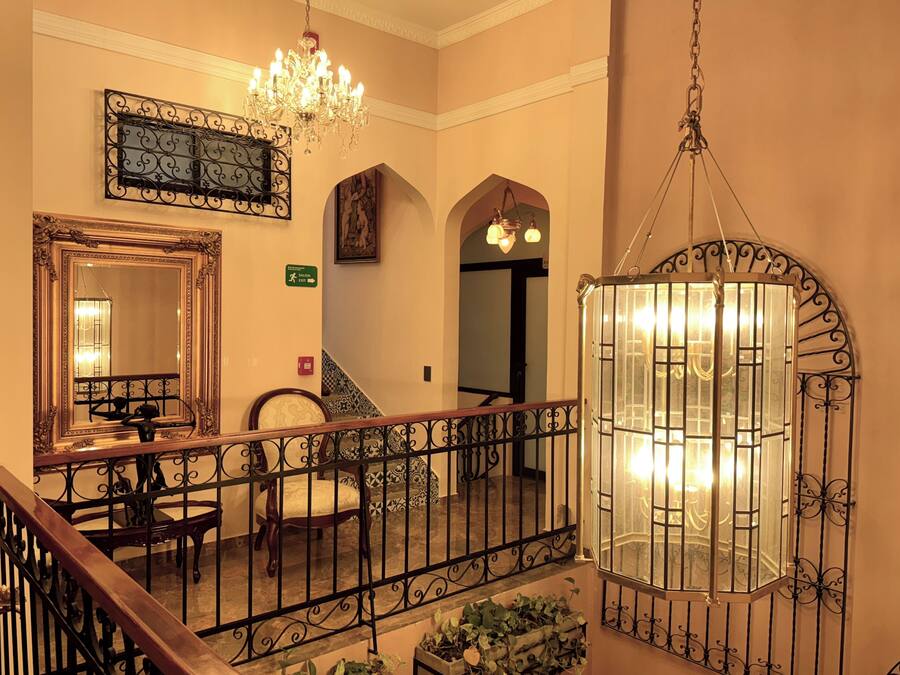 Un'imponente scalinata con ringhiere in metallo finemente decorate, un lampadario e un grande specchio.