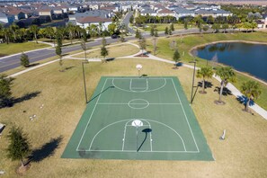 Vue aérienne d’un terrain de basketball entouré d’un quartier résidentiel avec des maisons, une route et une étendue d’eau.