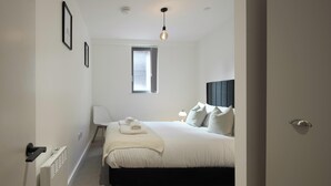 A bedroom with a bed, a window, a radiator, a chair, and a bedside table. - Stylish Northern Quarter Sanctuary (Manchester)