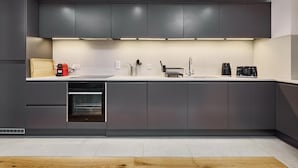 A modern kitchen with grey cabinets, a built-in oven, a sink, and a coffee maker. - Stylish Northern Quarter Sanctuary (Manchester)
