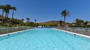 A clear blue pool with a blue border, surrounded by palm trees and lounge chairs.
