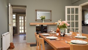 A dining area with a wooden table set for four, a vase with flowers, and a mirror above the table.