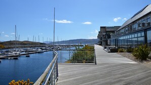 A marina with boats docked, a wooden walkway, and a modern building with large windows.