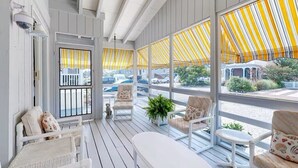 A covered porch with white wicker furniture, yellow-striped awnings, and a view of parked cars and greenery outside. - Town of Bethany Beach- one block from beach (Bethany Beach)