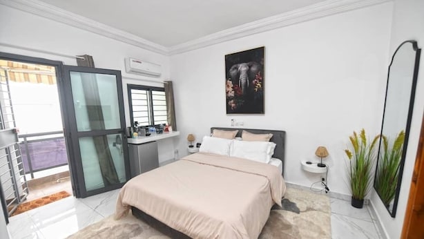 Un dormitorio moderno con una cama grande, una puerta de vidrio que da a un balcón y un aire acondicionado instalado en la pared.