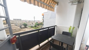 Un balcón con mesa y sillas, vista de los edificios circundantes y un extintor rojo en la pared.