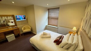 A hotel room with a bed, a desk, a chair, a TV, and a window with blinds. - George Hotel Hayfield (High Peak)