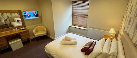 A hotel room with a bed, a desk, a chair, a TV, and a window with blinds.