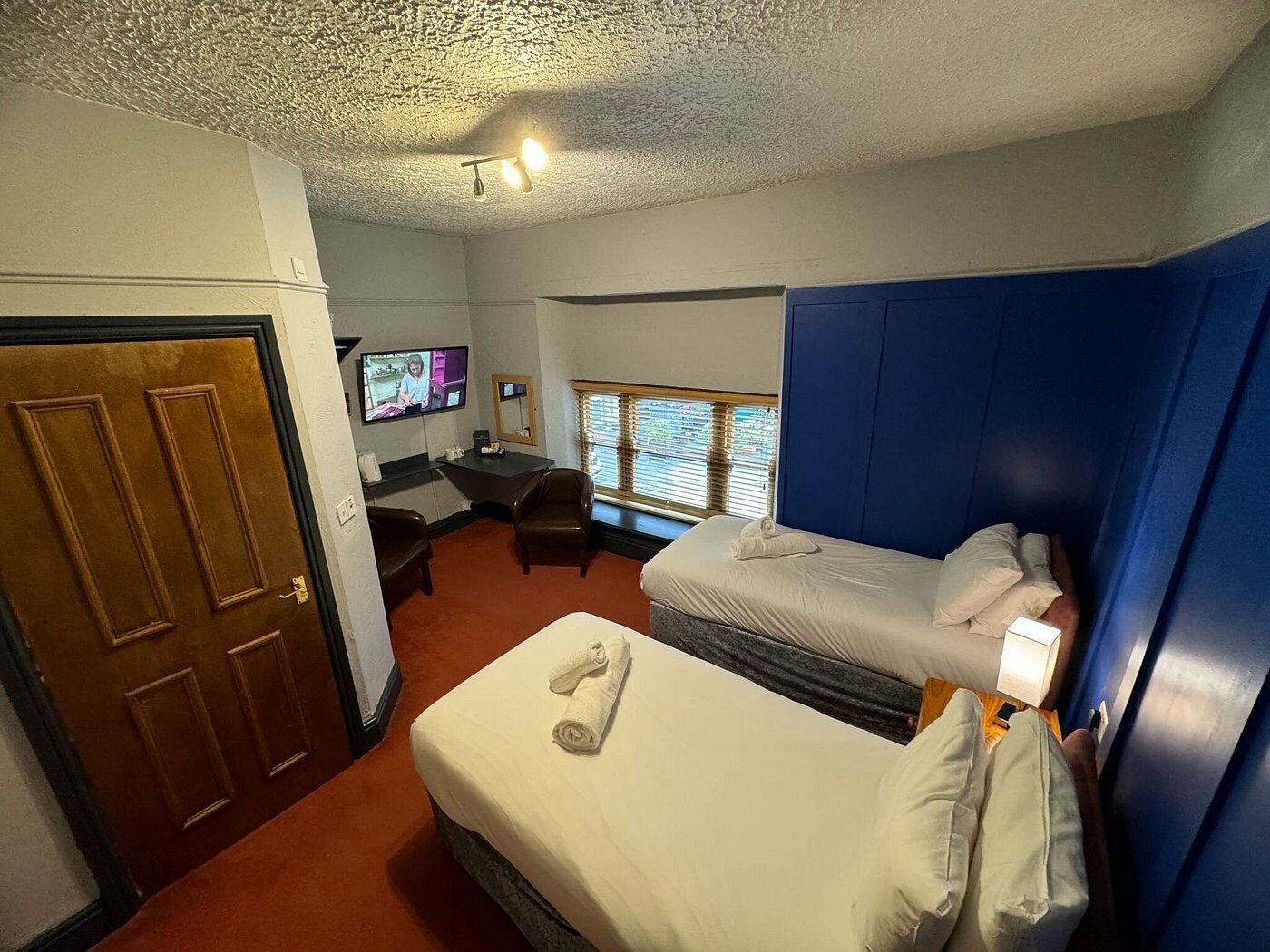 A hotel room with two beds, a desk, a television, and a window with blinds.