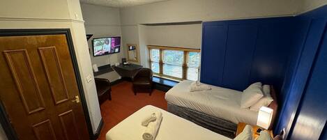 A hotel room with two beds, a desk, a television, and a window with blinds.