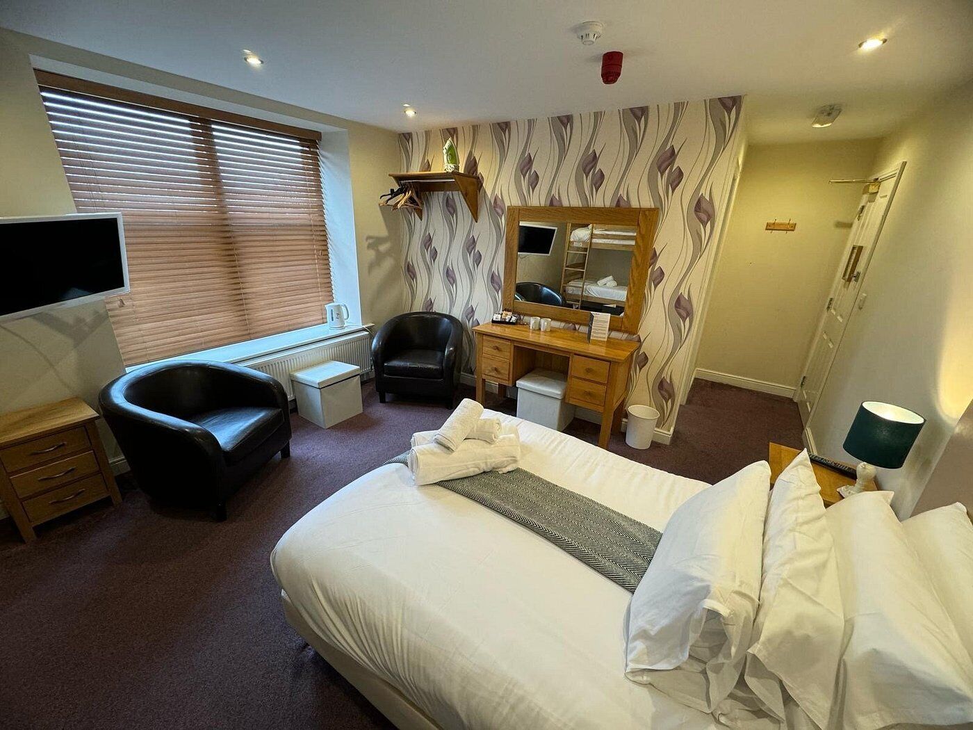 A hotel room with a bed, a desk, a chair, a TV, a bathroom, and a window with blinds.
