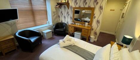 A hotel room with a bed, a desk, a chair, a TV, a bathroom, and a window with blinds.