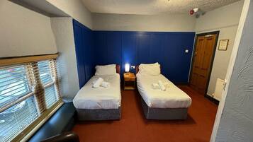 A hotel room with two beds, a window with blinds, a wooden door, and a radiator.