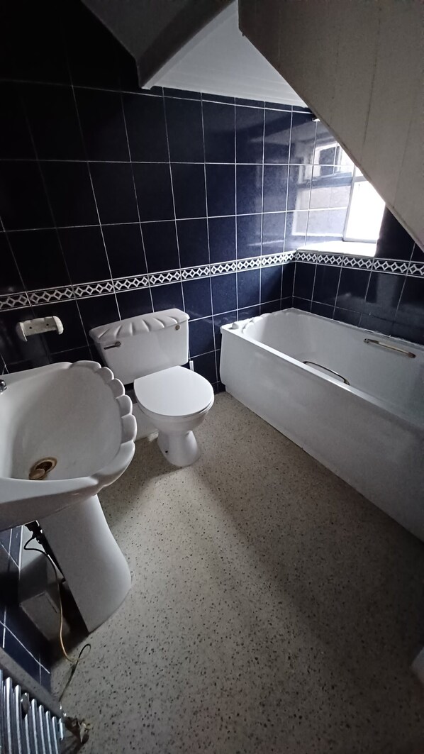 Un baño con inodoro, lavamanos y bañera, todos en color blanco.