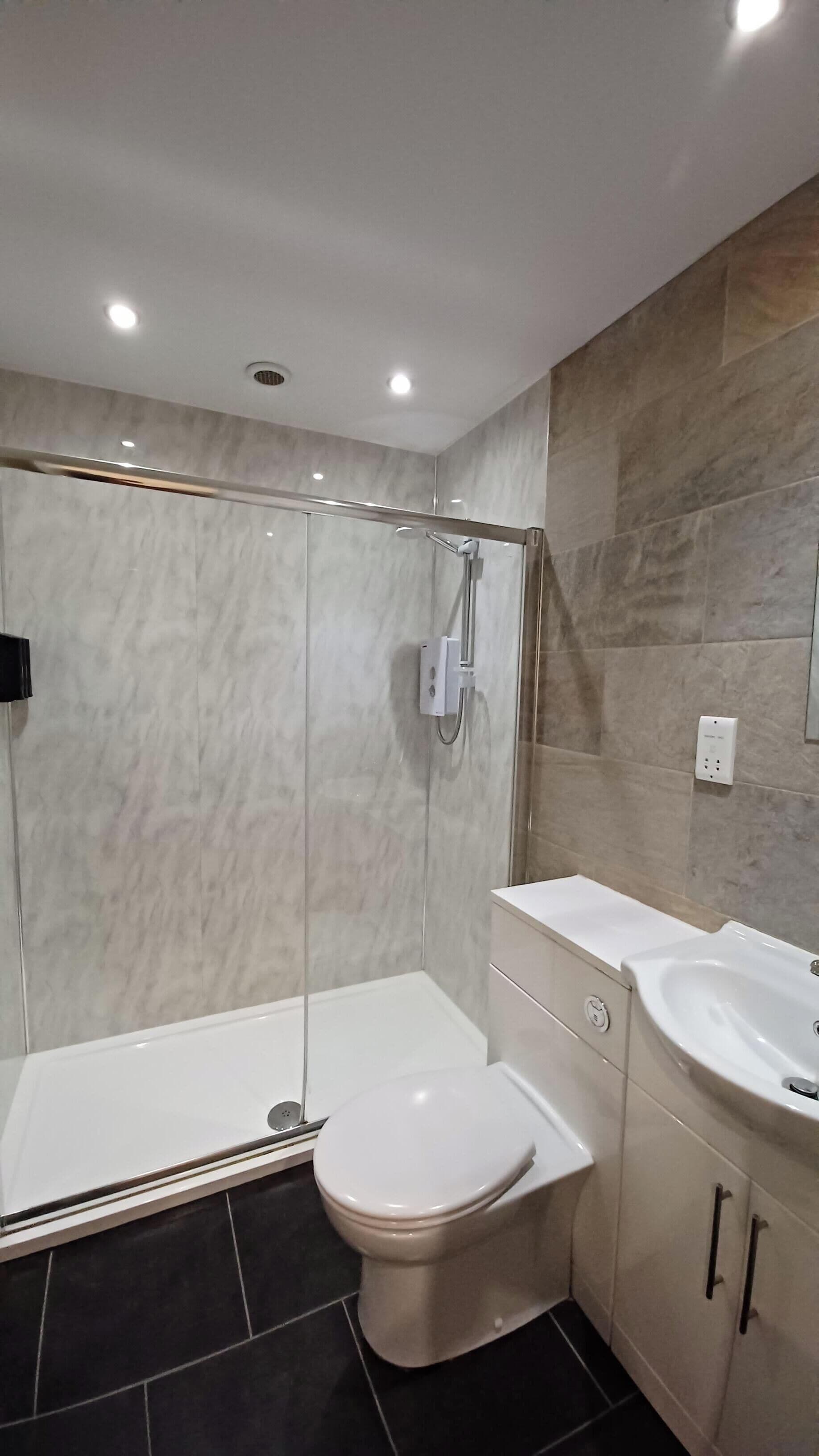 Une salle de bain moderne avec une douche à parois de verre, des toilettes blanches et un meuble-lavabo.