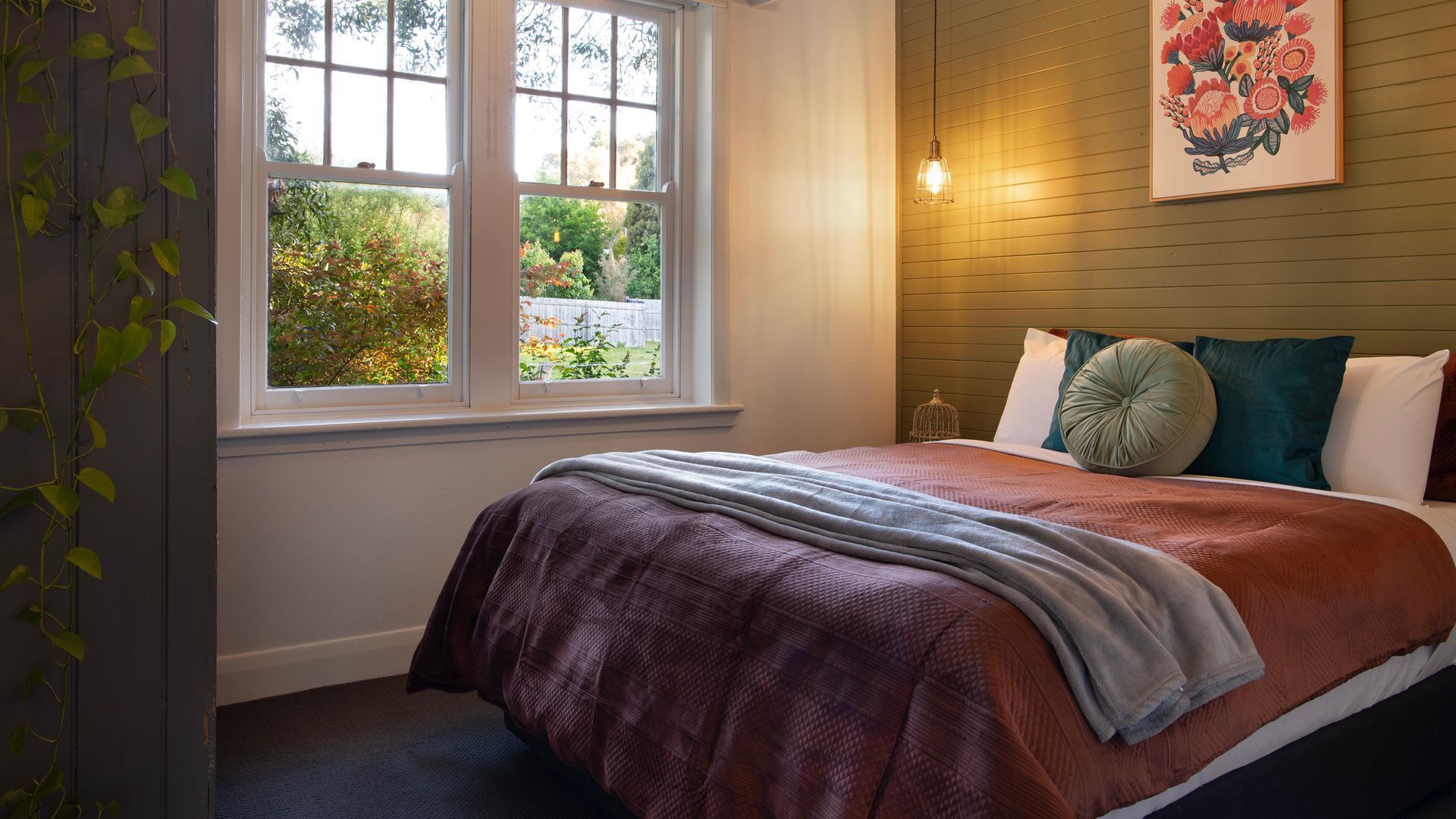 Una camera da letto con un letto, una finestra, una lampada a parete e un quadro con fiori.