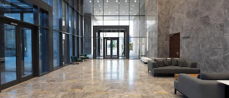 Un hall d’entrée spacieux au design moderne, agrémenté d’un grand lustre, d’un coin salon avec des canapés et d’une entrée en verre.