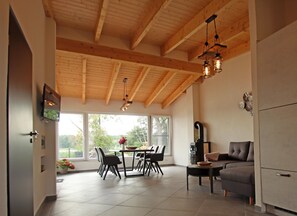 Eine geräumige Küche mit Holzbalken, eine Essecke mit Stühlen und einem Tisch sowie eine Sitzecke mit einer Couch.