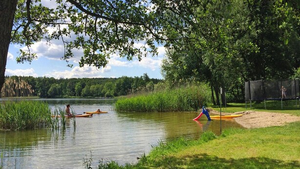 A lakeside setting with kayaks, a sandy area with a slide, and a playground. - Bungalow in Klein Labenz for 4 Personen (Warin)