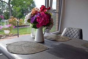 Een eettafel met een bloevas, twee placemats en uitzicht op een tuin door een raam.
