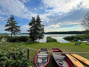 Uitzicht op een meer met twee aanmeren kanoto's, een gazon en bomen.