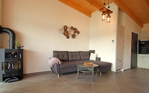 A living room with a sofa, a small round table, a decorative wall piece, a fireplace, and a kitchen area. - Holiday Apartment With Private Lake Access and Jetty (Warin)