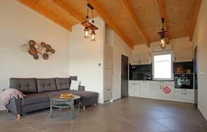 A modern living room with a sofa, a round coffee table, and a kitchen area with cabinets and a refrigerator.