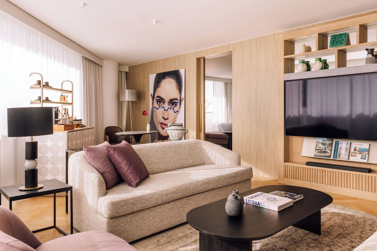 Een moderne woonkamer met een bank, salontafel en een flatscreen televisie. Er is een boekenkast met decoratieve items en een groot schilderij aan de muur.