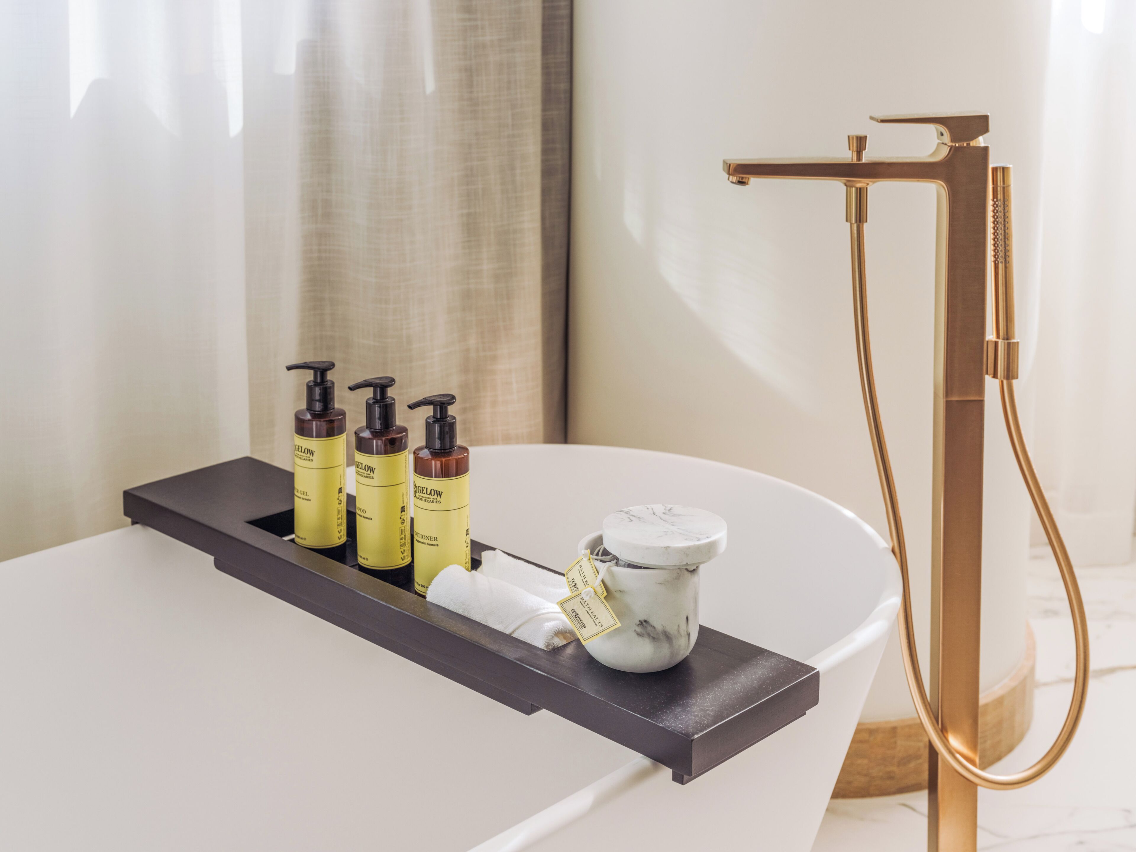 A bathroom with a white sink, a gold faucet, and three bottles of gel on a shelf.
