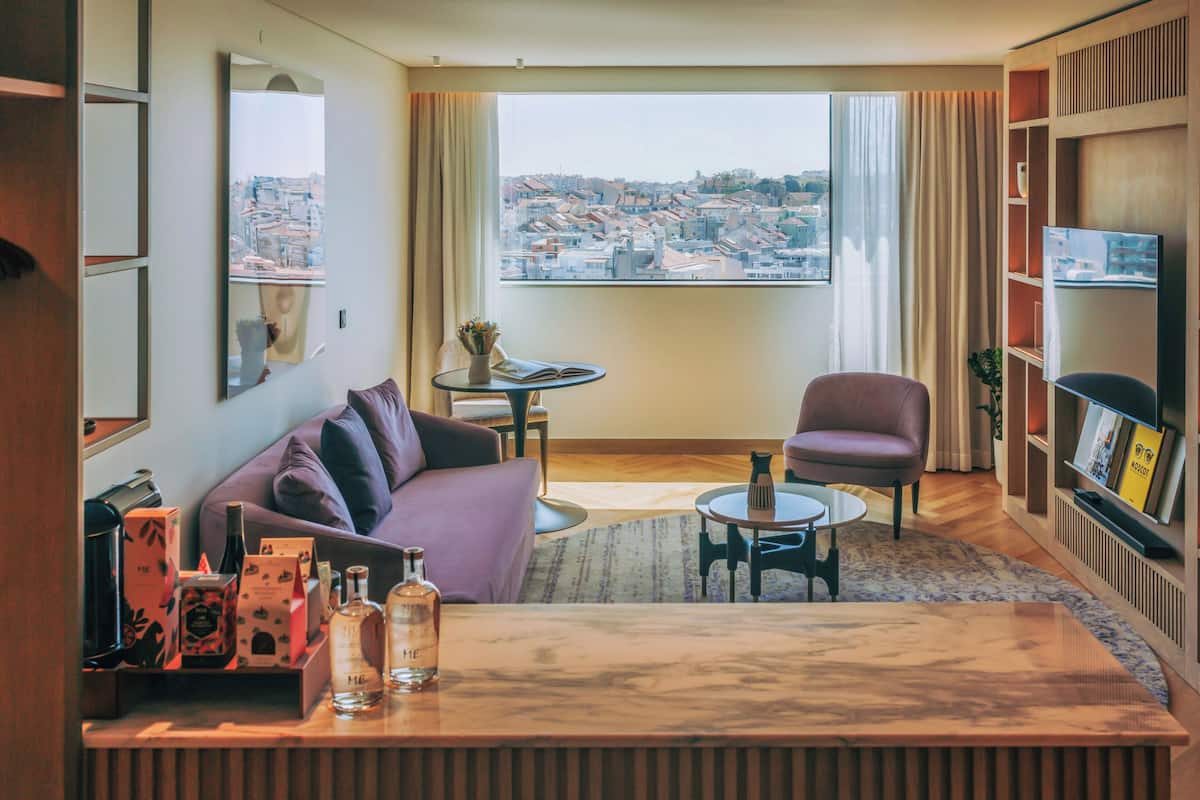 Een moderne woonkamer met een bank, fauteuil, salontafel en uitzicht op een stadsgezicht door een groot raam.