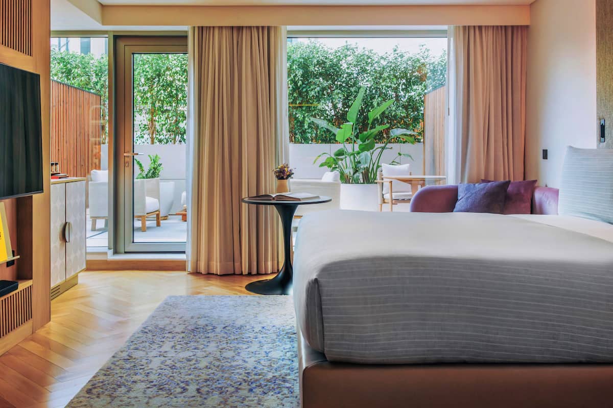Een moderne hotelkamer met een groot bed, een televisie, een tafeltje en een balkon met gordijnen.