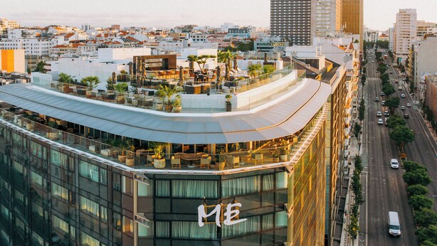 Un hôtel moderne doté d’une façade incurvée en verre, d’un jardin sur le toit et d’un grand panneau en forme de « M ».