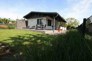 Ein modernes Haus mit einer Terrasse, einem Grill und einem überdachten Sitzbereich im Freien.