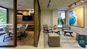 A modern office space with a meeting area, comfortable seating, a large artwork, and a view through a glass door. - 2 Bedroom Apartment with Sea View Rooftop (Salvador)