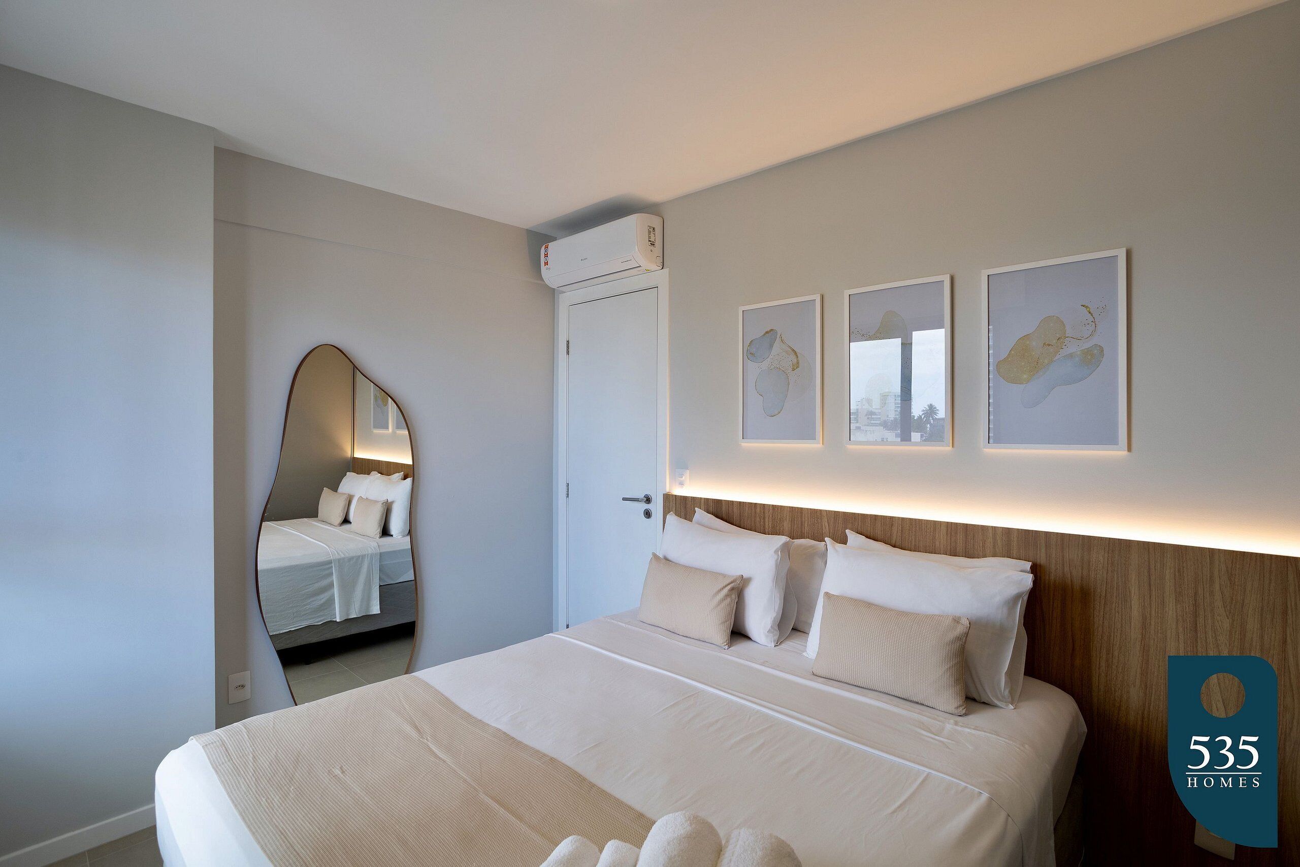 A modern hotel room with a large bed, a mirror, and three framed artworks on the wall.