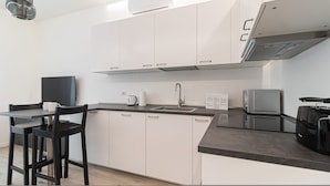 A modern kitchen with white cabinets, a black countertop, a sink, a kettle, a microwave, and a television. - Italianway - Serra 16 (Milan)