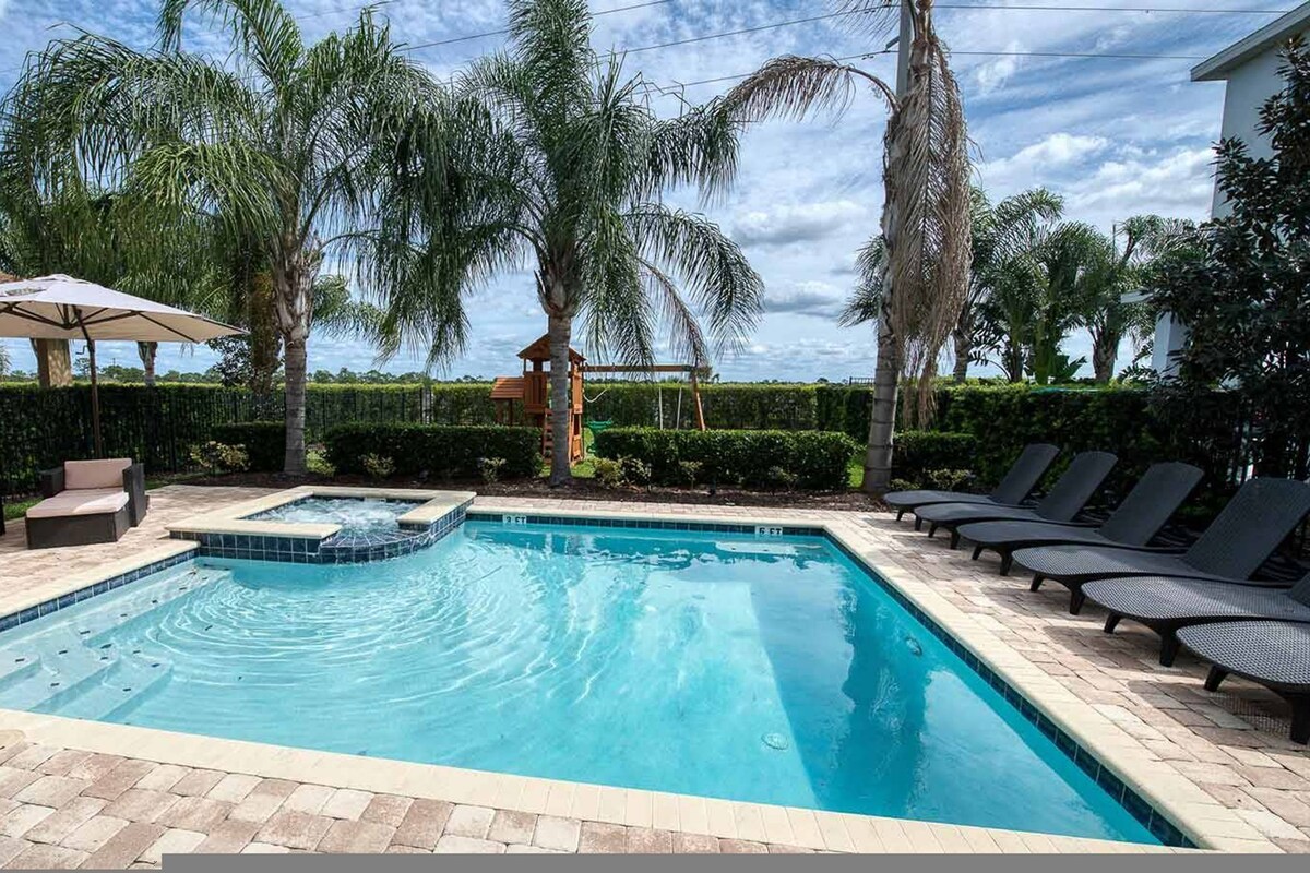 Una piscina rectangular con un jacuzzi, rodeada de sillones y un sofá.
