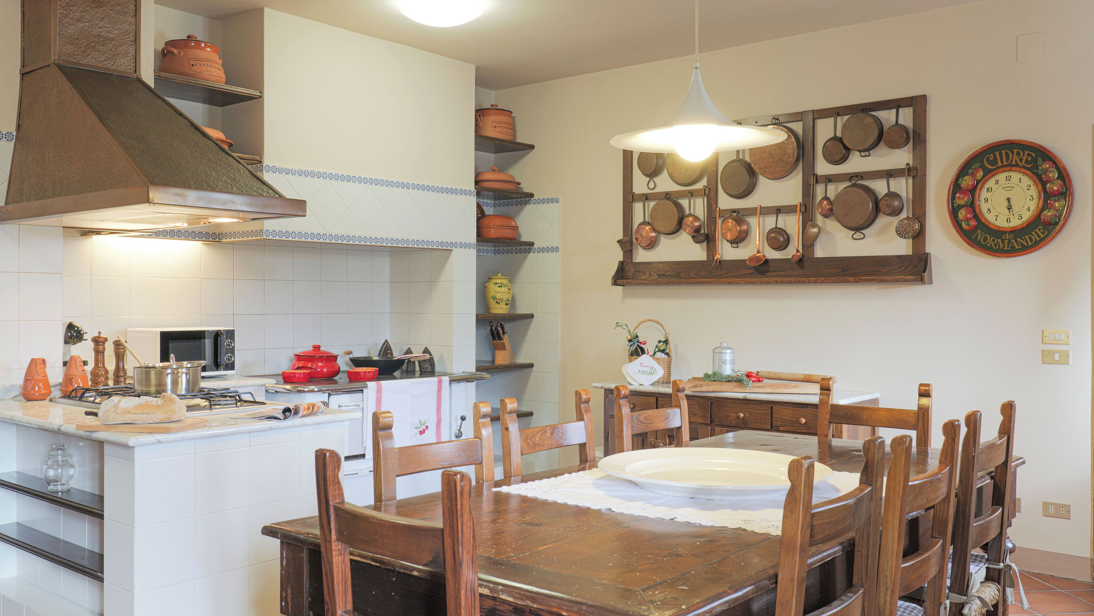 A kitchen with a central island, wooden chairs, a dining table, and a clock on the wall.