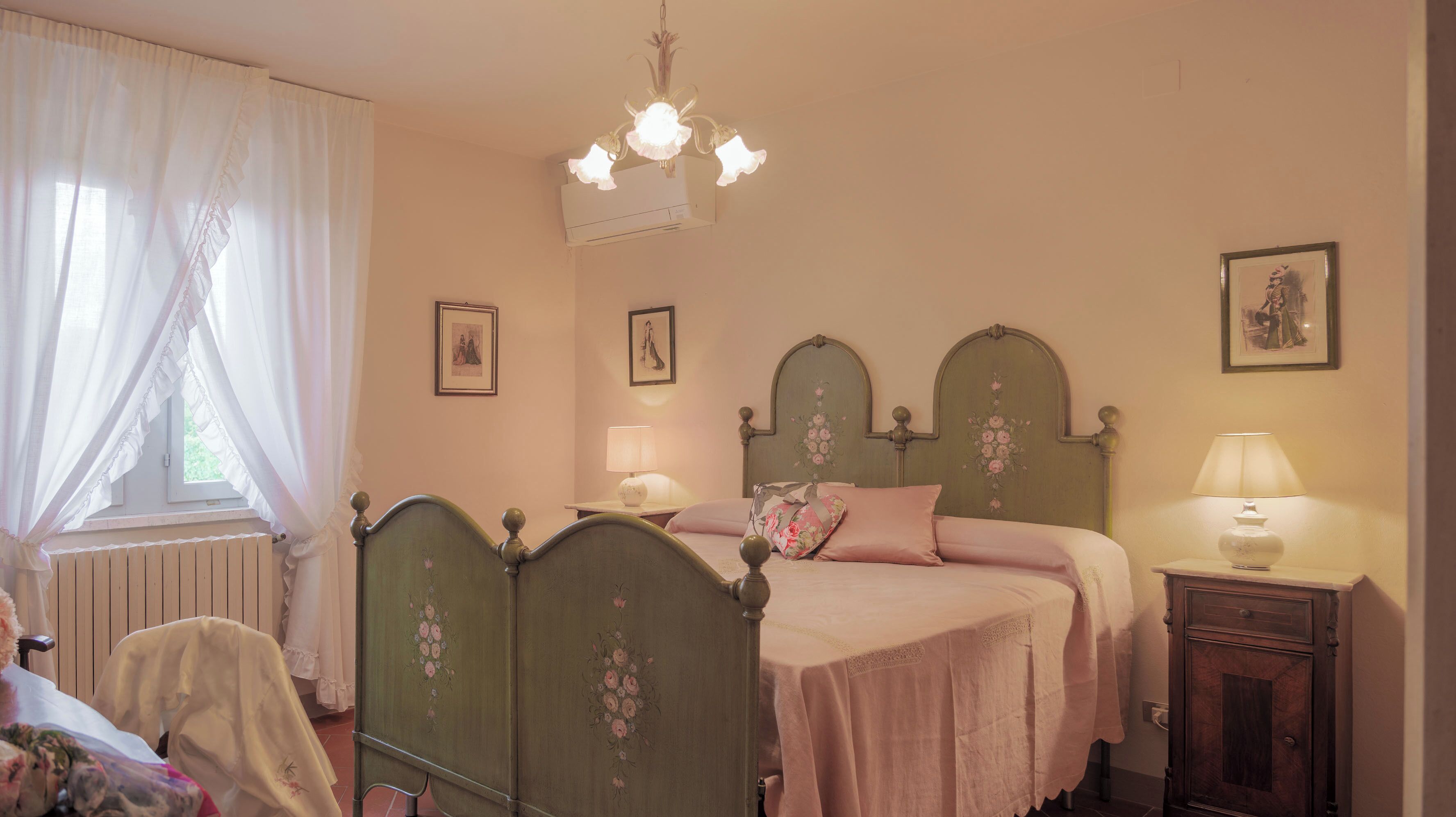 Une chambre à coucher comprenant un lit, deux tables de chevet, une fenêtre avec des rideaux, un radiateur et un lustre.