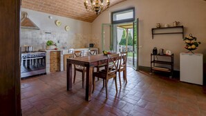 A spacious kitchen with a brick ceiling, a dining table with chairs, a built-in oven, and a hanging light fixture. - Villa Iside 8, Emma Villas (Peccioli)