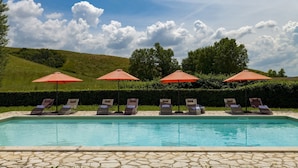 A swimming pool with lounge chairs and umbrellas, surrounded by a stone patio and greenery. - Villa Iside 8, Emma Villas (Peccioli)