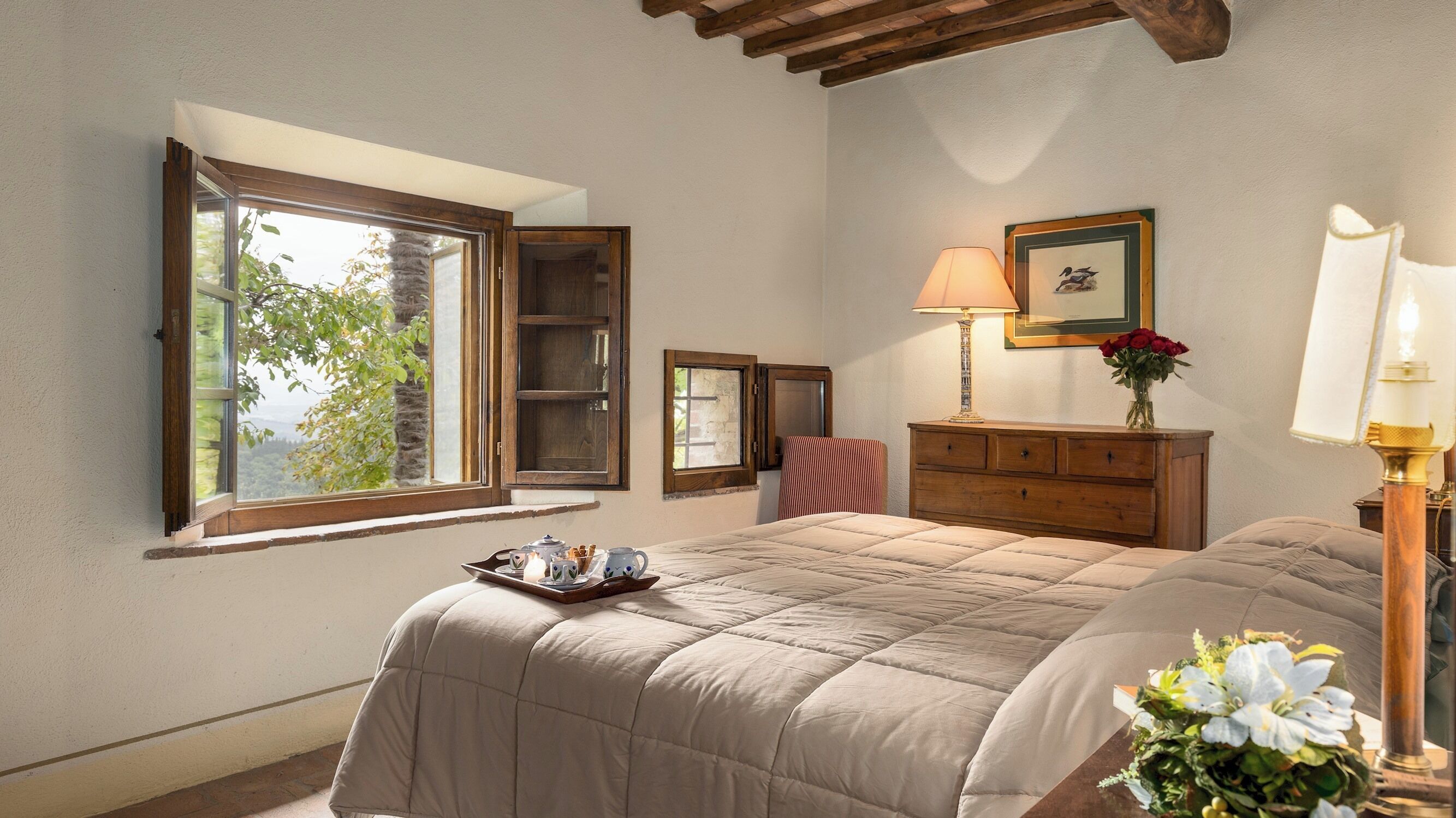 Une chambre à coucher avec un grand lit, une commode, une fenêtre donnant sur un beau paysage, une lampe et un tableau encadré au mur.