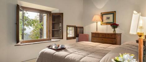 Une chambre à coucher avec un grand lit, une commode, une fenêtre donnant sur un beau paysage, une lampe et un tableau encadré au mur.