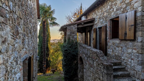 A narrow stone corridor with a wooden door and steps leading to a building with a stone wall and wooden shutters. - Castellare in Poggio 10, Emma Villas (Castellina in Chianti)