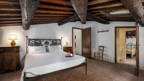 Une chambre à coucher avec un lit en bois, deux tables de chevet avec des lampes, une chaise et une porte donnant sur une autre pièce.