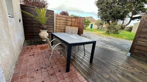 Une terrasse extérieure avec une table et des chaises, un pot de fleurs et une clôture en bois.