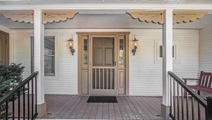 A porch with a wooden door, two wall-mounted lights, and a bench.