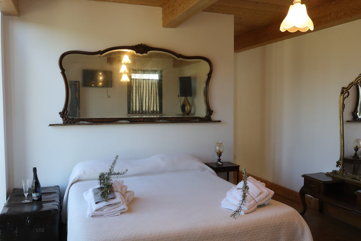 A neatly made bed with folded towels, a large ornate mirror, and a bedside table with a lamp.