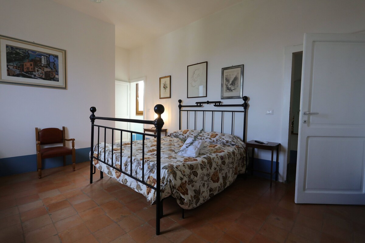 A bedroom with a bed, a chair, a bedside table, and a door.