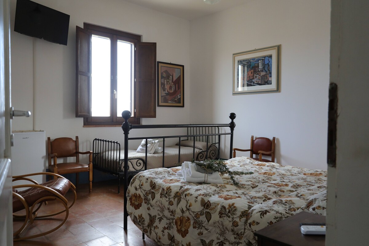 A bedroom with a bed, two chairs, a window, and artwork on the walls.